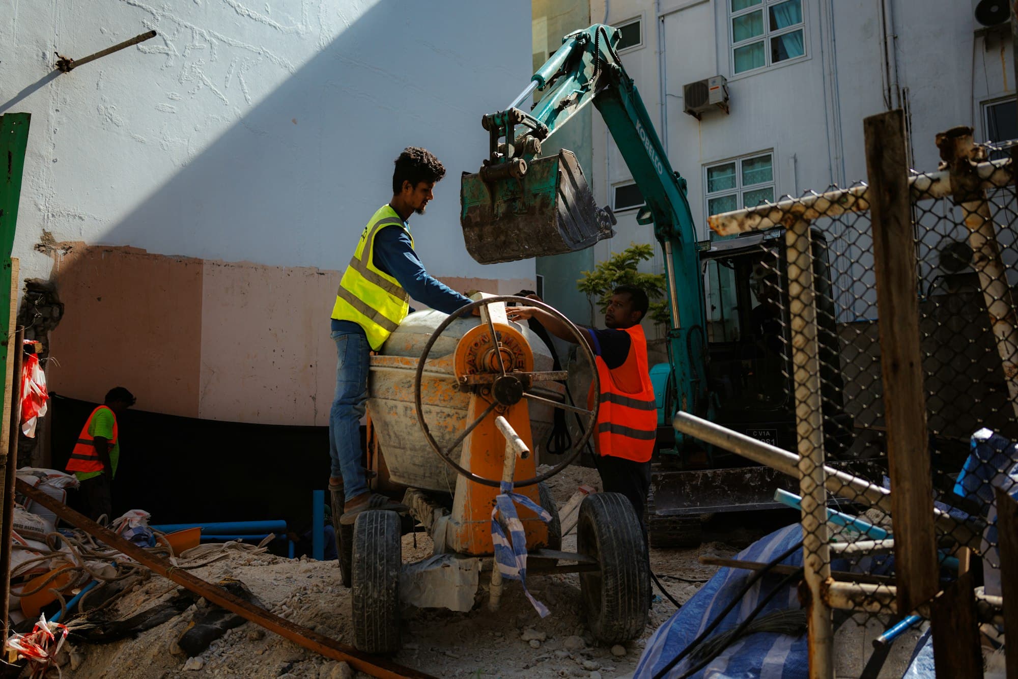 Construction workers in high-visibility vests operating a cement mixer